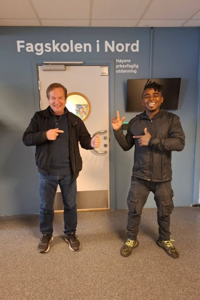 Bilde av to menn som står i en gang. På veggen bak dem står det "Fagskolen i Nord Høyere ykesfaglig utdanning". 