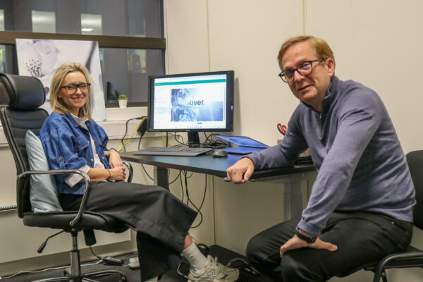 Bilde av en kvinne og en mann som sitter ved en skriveput inne på et kontor. På dataskjermen i bakgrunnen står det #Livet