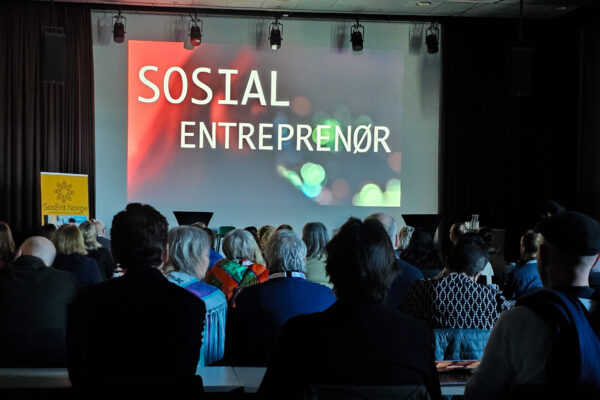 Fullt konferanselokale. På lerretet står det: sosial entreprenør